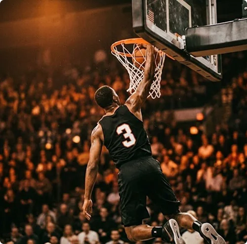Un basketteur vêtu d'un maillot noir, numéro 3, en plein saut, en train de réaliser un dunk. La foule est floue à l'arrière-plan ; une photo d'action pleine de vie et de dynamisme.